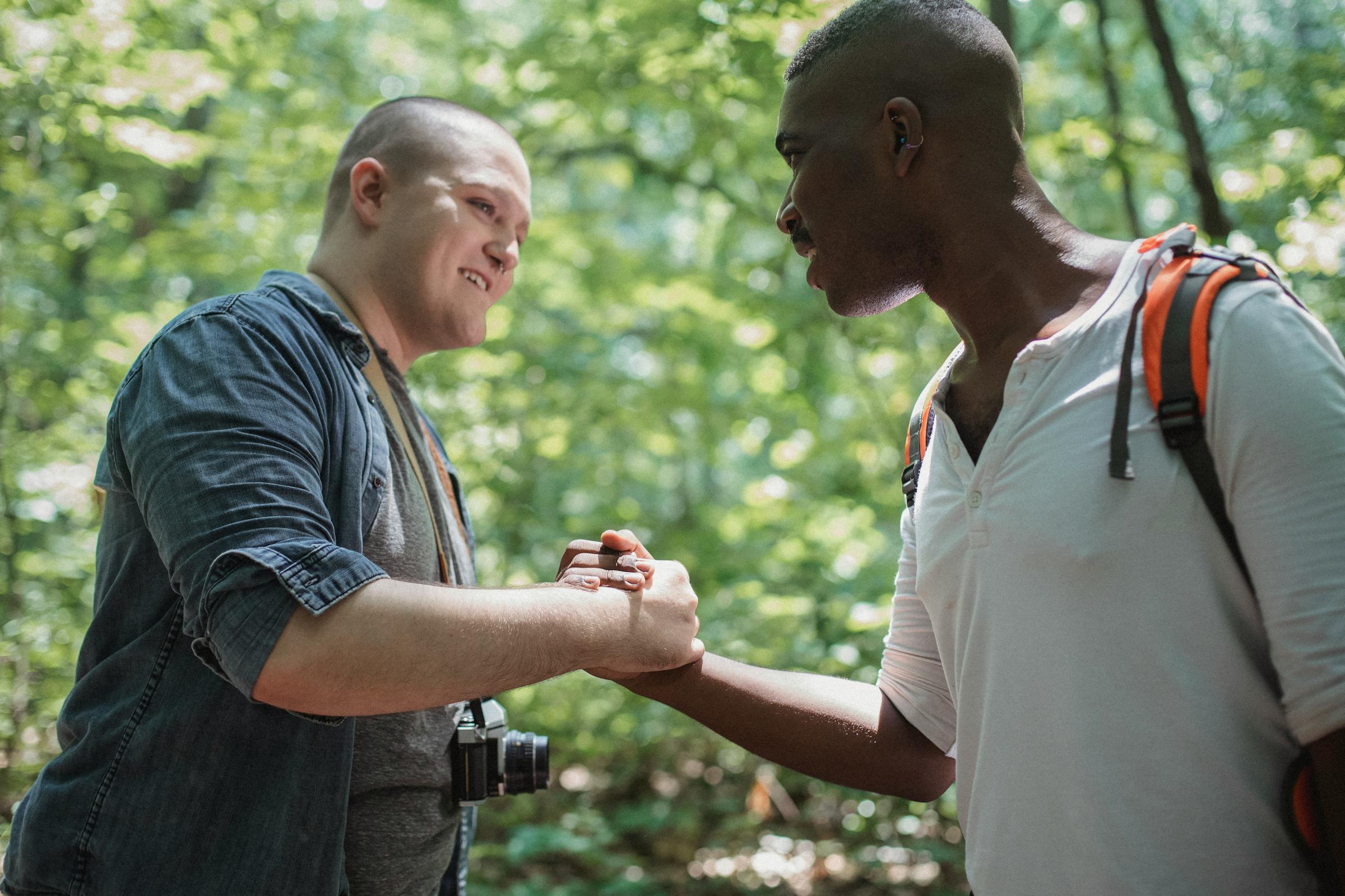Two diverse men sharing a warm handshake outdoors, smiling in a natural setting
